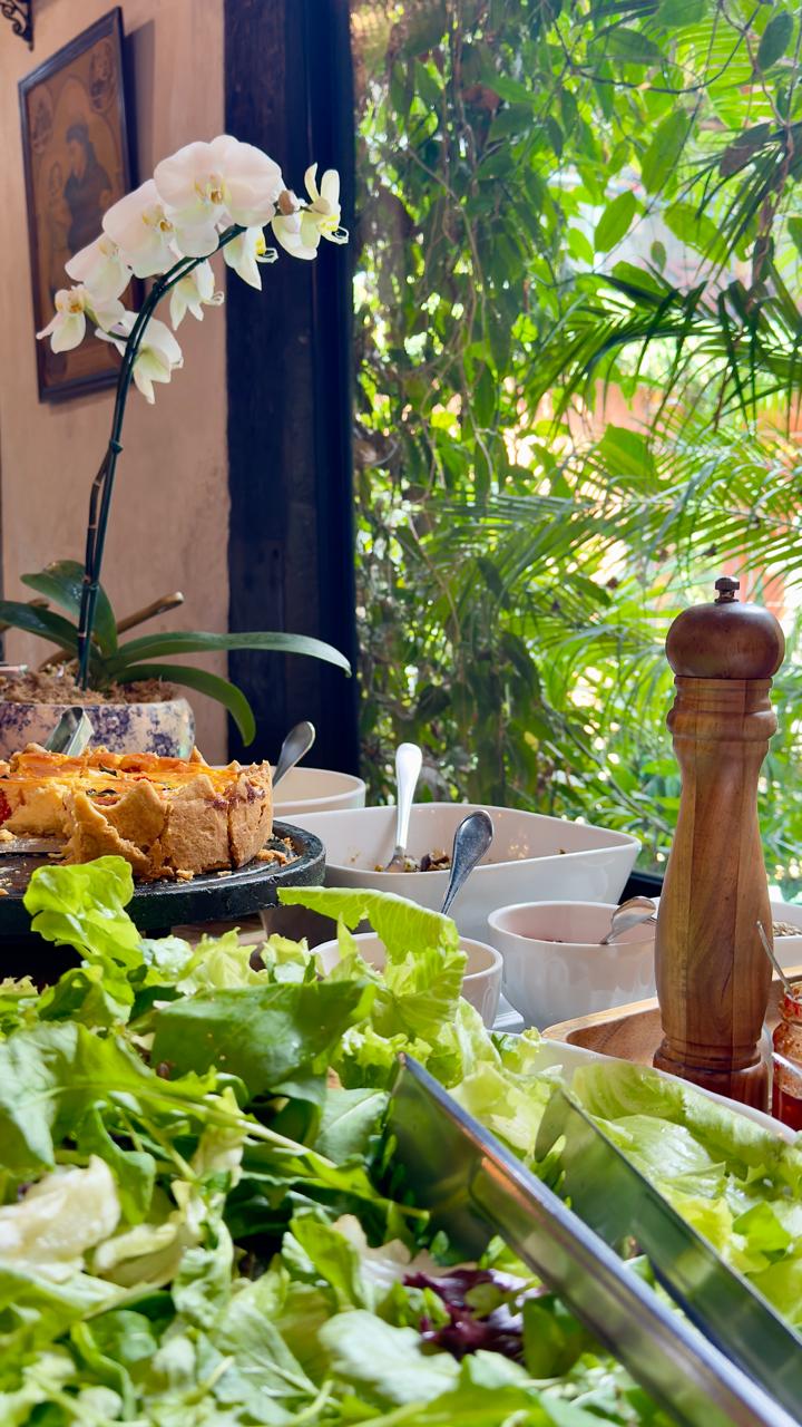 Mesa de restaurante com salada e quiche em ambiente arborizado